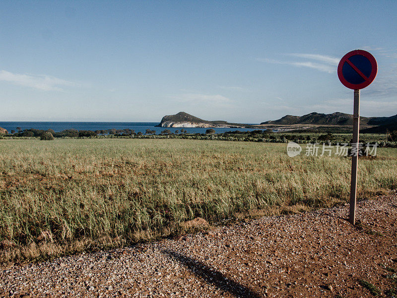 在西班牙阿尔梅里亚的一个小镇“Cabo de Gata”，可以看到远处一条长满干草和小山的干旱道路。